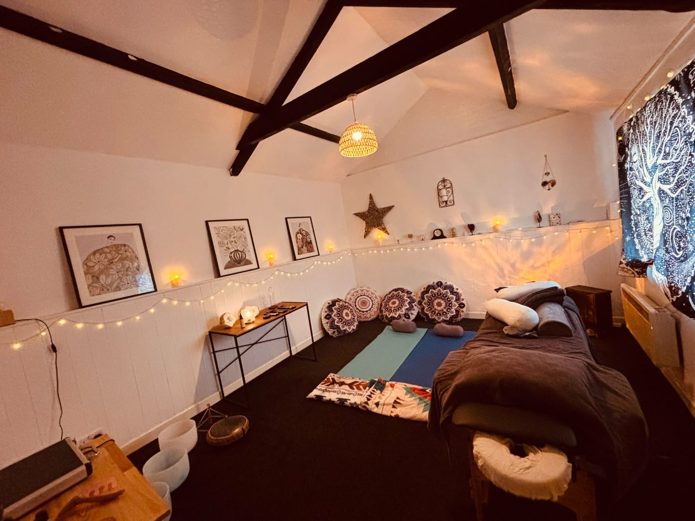 The Stable Sanctuary treatment room with a massage table, floor cushions, sound bowls and soft fairy lights.
